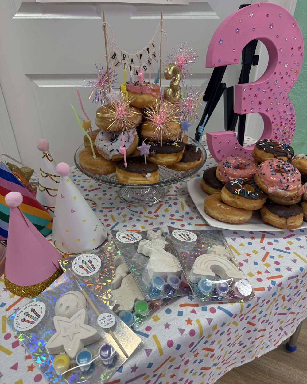 A birthday table with a donut tower, a pink number 3 and Three Tiny Brushes party packs in the foreground